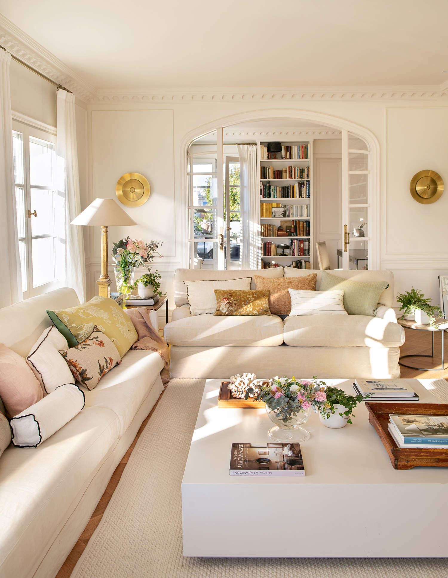 Salón elegante y luminoso con sofás blancos y apliques dorados. 